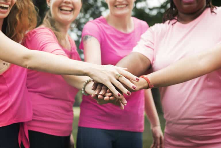 mulheres com blusa rosa com as mãos juntas representando o que é outubro rosa