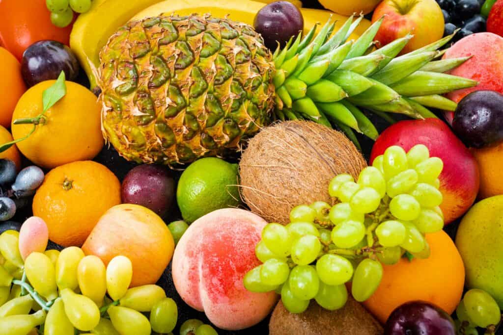 Texto Alternativo - Na imagem há diversas frutas juntas: abacaxi, uva, laranja, uvas verdes, ameixas.