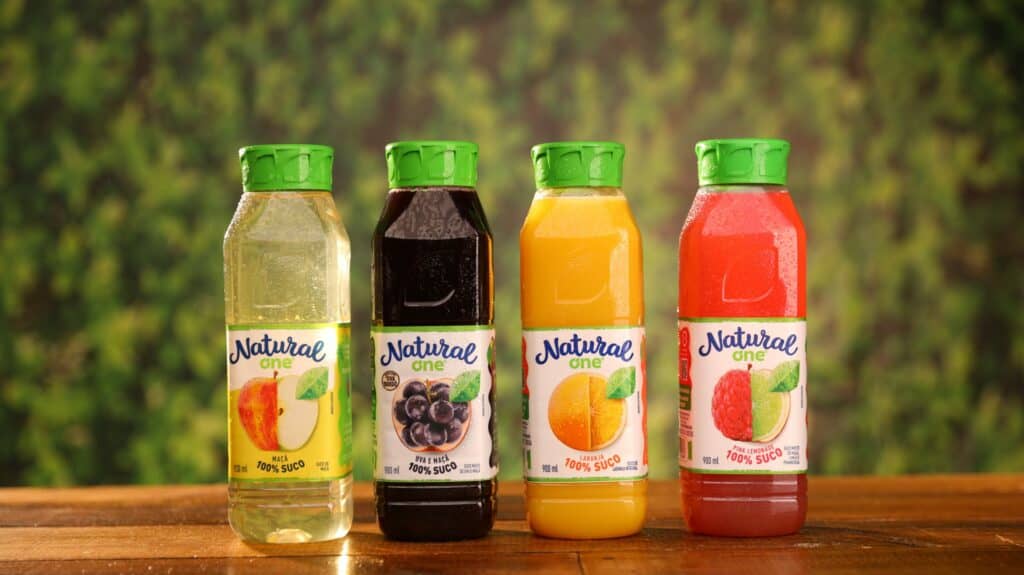 Texto Alternativo: Na imagem há quatro embalagens de sucos Natural One nos sabores maçã, uva, laranja e pink lemonade.
