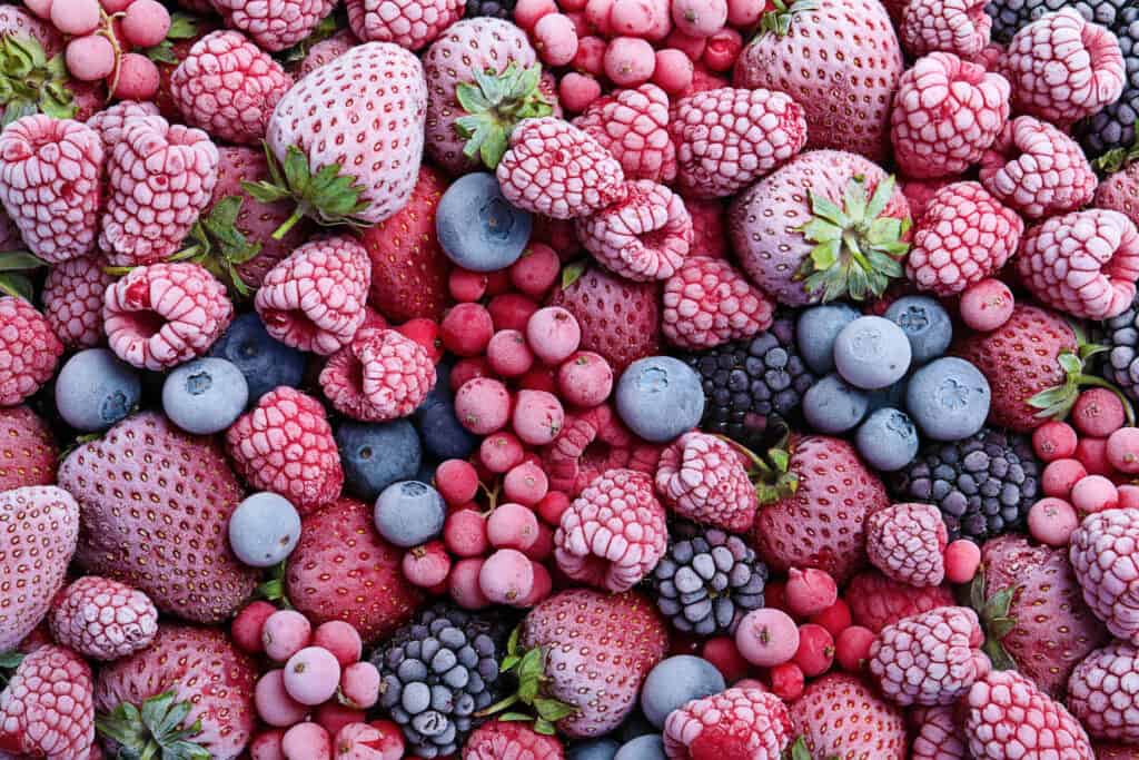 Na imagem há diversas frutas vermelhas, como morango, framboesa, cereja, congelados.