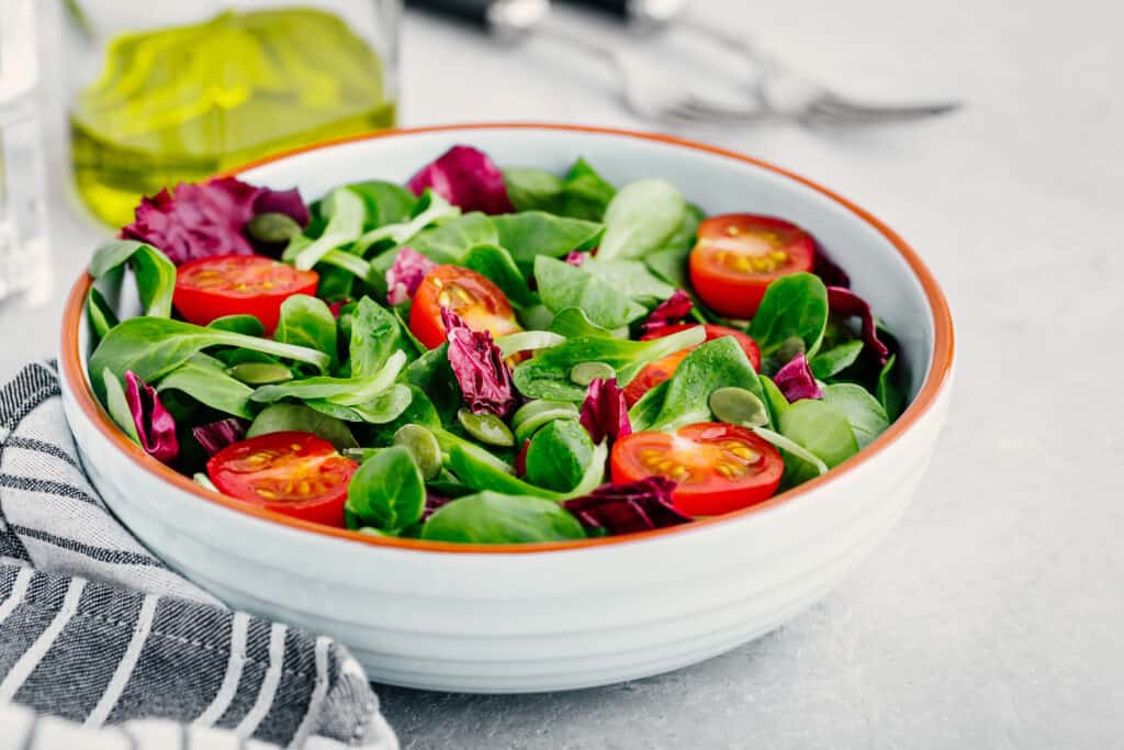 Texto alternativo: na imagem há um bowl branco, de cerâmica, com folhas de rúcula verdes e tomates cerejas cortados ao meio. 