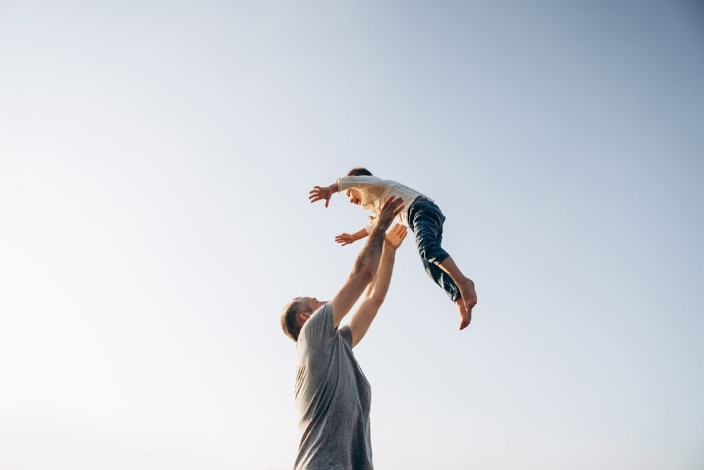 na imagem há um homem, representando um pai no dia dos pais, levantando uma criança.