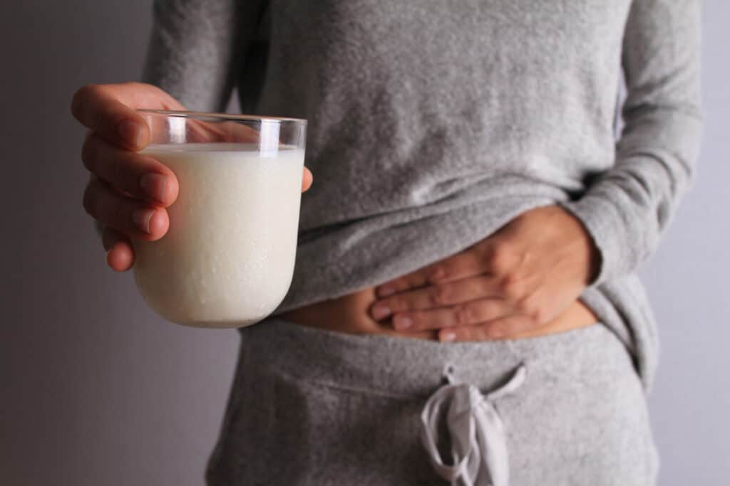 Texto alternativo: Na imagem há uma mulher com moletom cinza segurando um copo de leite em recipiente transparente