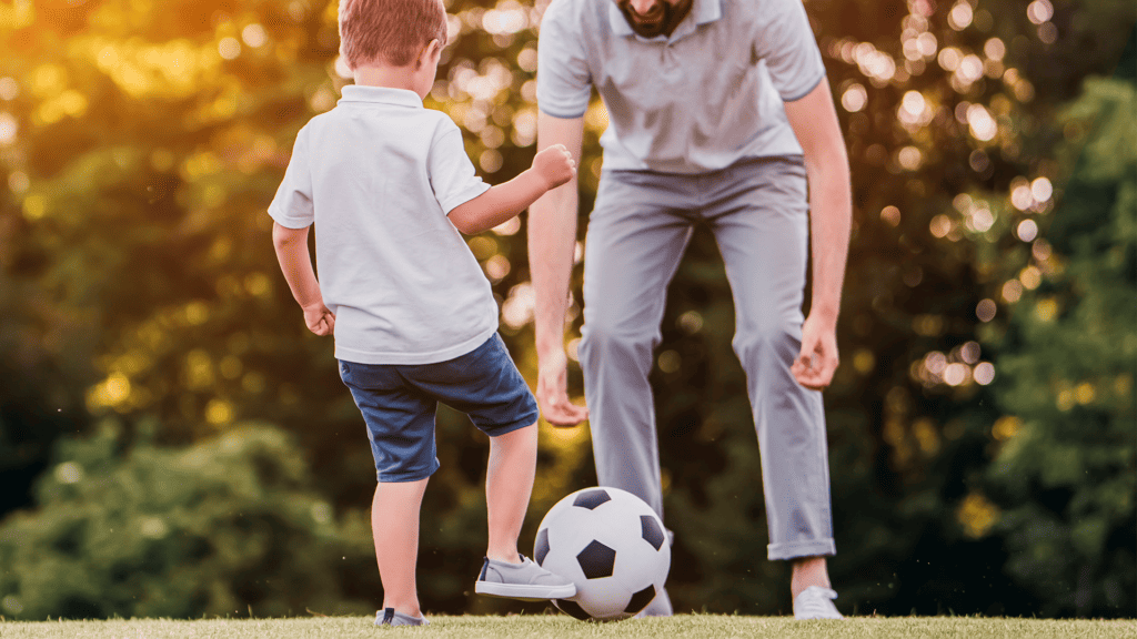 Na imagem há um homem jogando bola com um menino