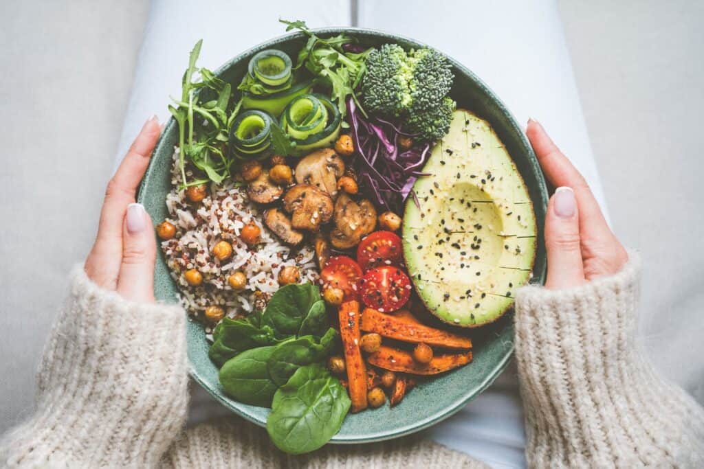 Na imagem há uma representação de alimentação saudável, que simboliza autocuidado. Na imagem, há um bol com diversos legumes cortados e cozidos, como cenoura, gão de bico, brócolis, pepino.