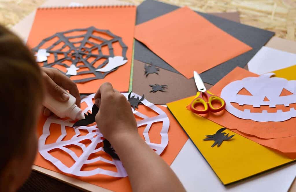 Texto alternativo: Na imagem há a mão de uma criança cortando decorações para o Halloween