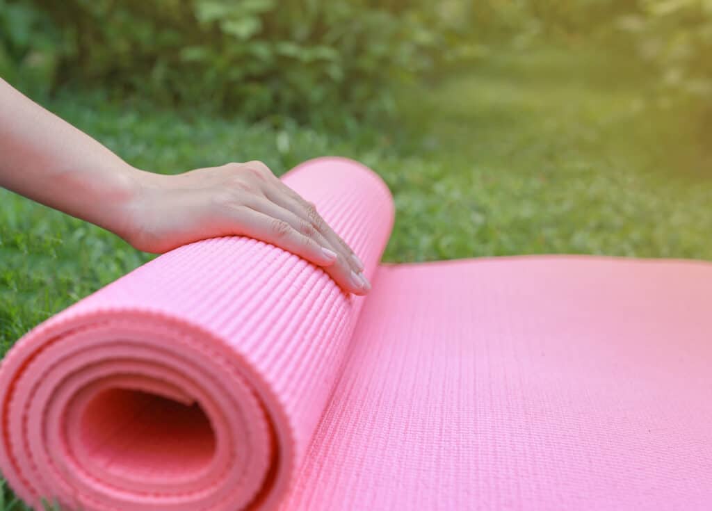 Texto alternativo: na imagem há uma mão sob um tapete de yoga rosa. A prática ajuda com a fortalecer contra o câncer de mama 