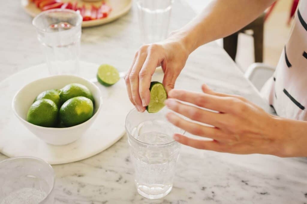 Na imagem há uma mão feminina espremendo limão em um copo com água