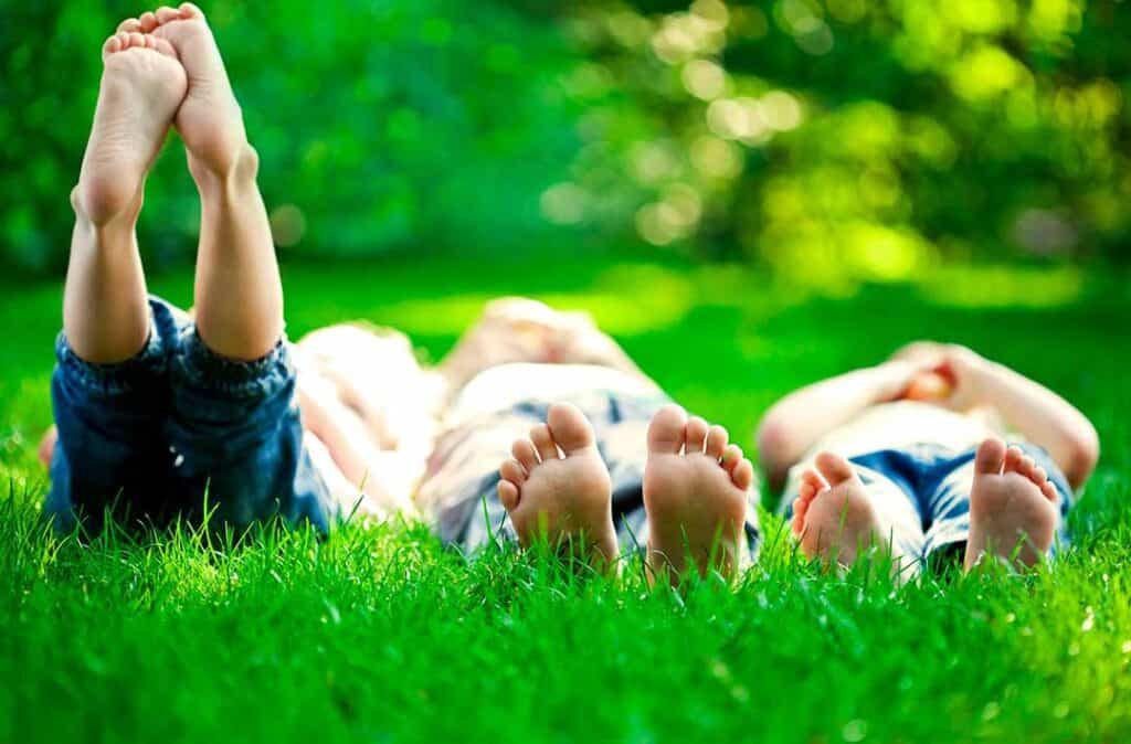 Texto alternativo: na imagem há três crianças deitadas na grama, como uma forma de aproveitar as férias