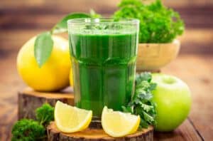 Texto alternativo - na imagem há um copo médio de vidro com suco verde detox. Ao lado do copo, uma maçã verde, e limões