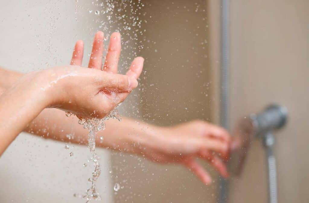 Texto alternativo: na imagem há uma mão, próxima a um chuveiro e a água está caindo