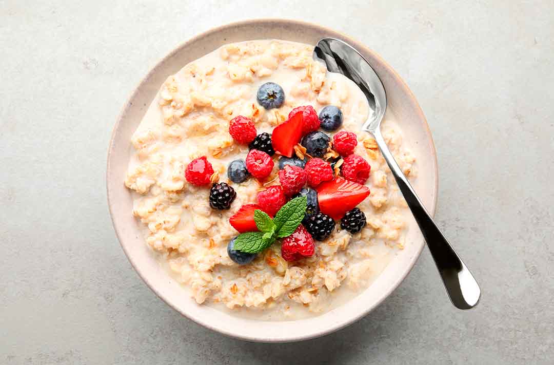 Texto alternativo: oatmeal, ou mingal de aveia gringo, com flocos de aveia e, no topo, frutas vermelhas. Também contém uma colher de metal