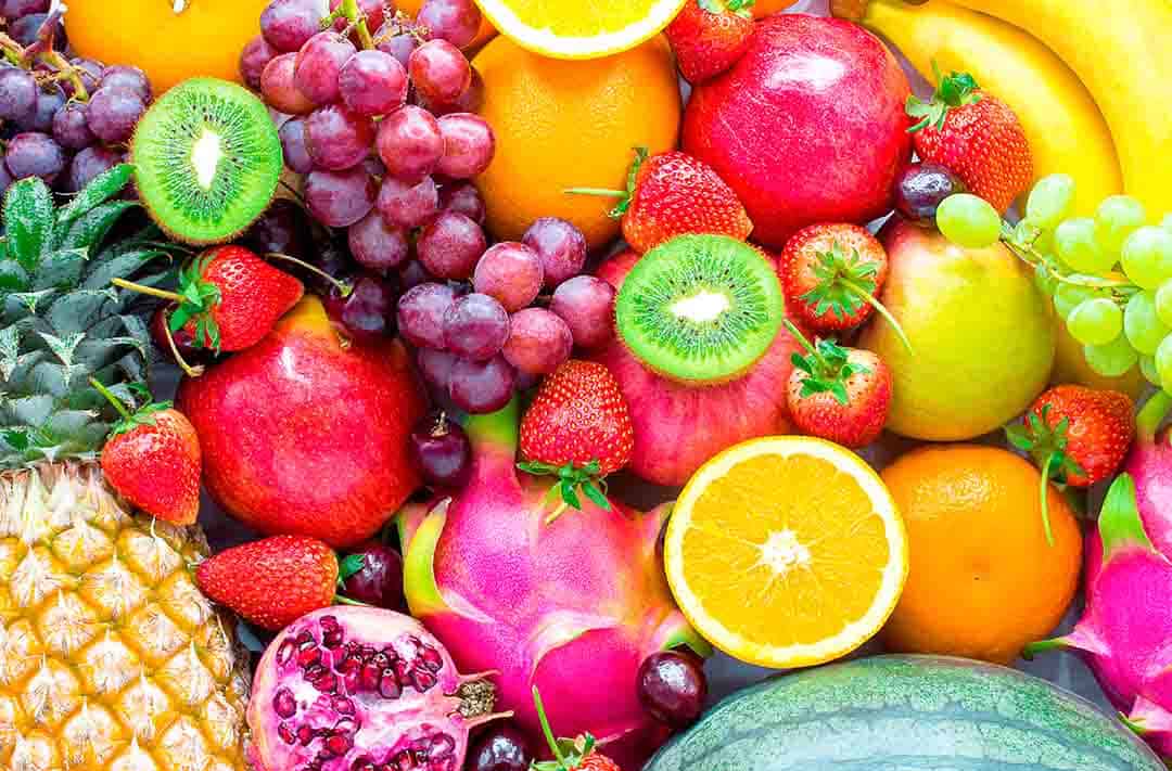 Texto alternativo: diversas frutas bem coloridas e misturadas, como: laranjas, kiwis, uvas e morangos