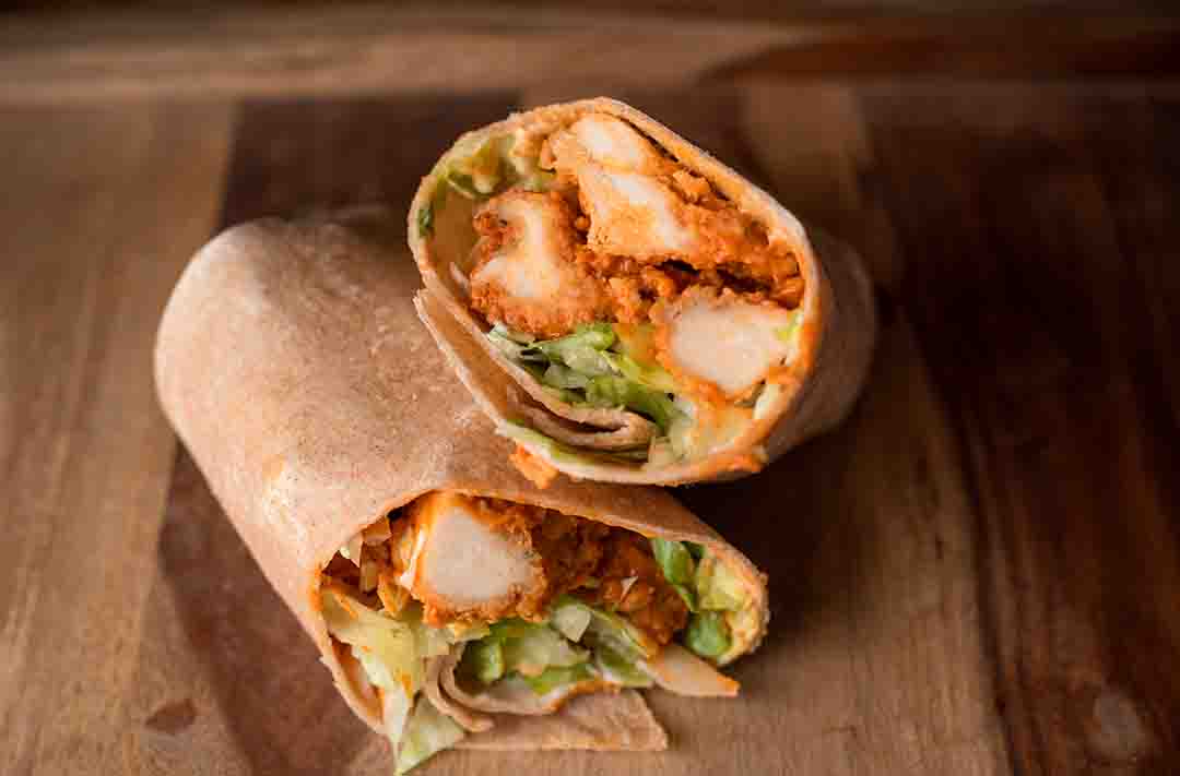 Texto alternativo: dois wraps recheados com frango e abacate sob uma mesa de madeira