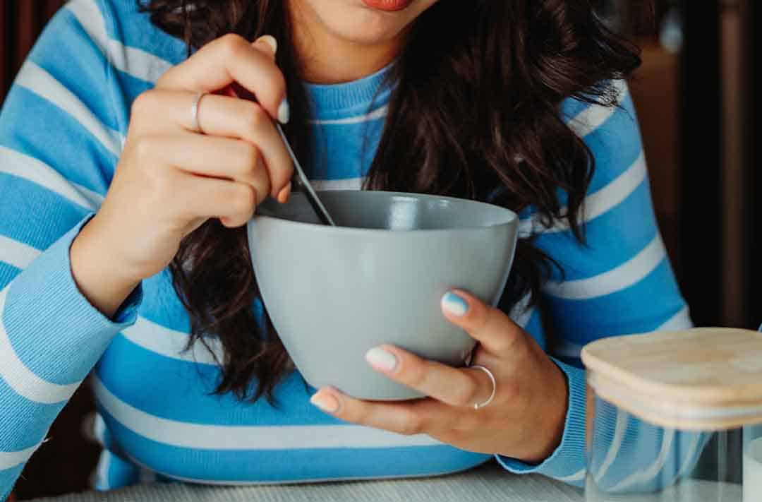 Texto alternativo: uma moça de blusa azul e branca listrada, comendo em um bowl azul